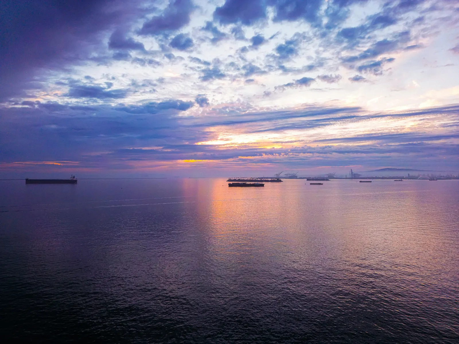 Ships waiting at anchor under dramatic clouds at sunset