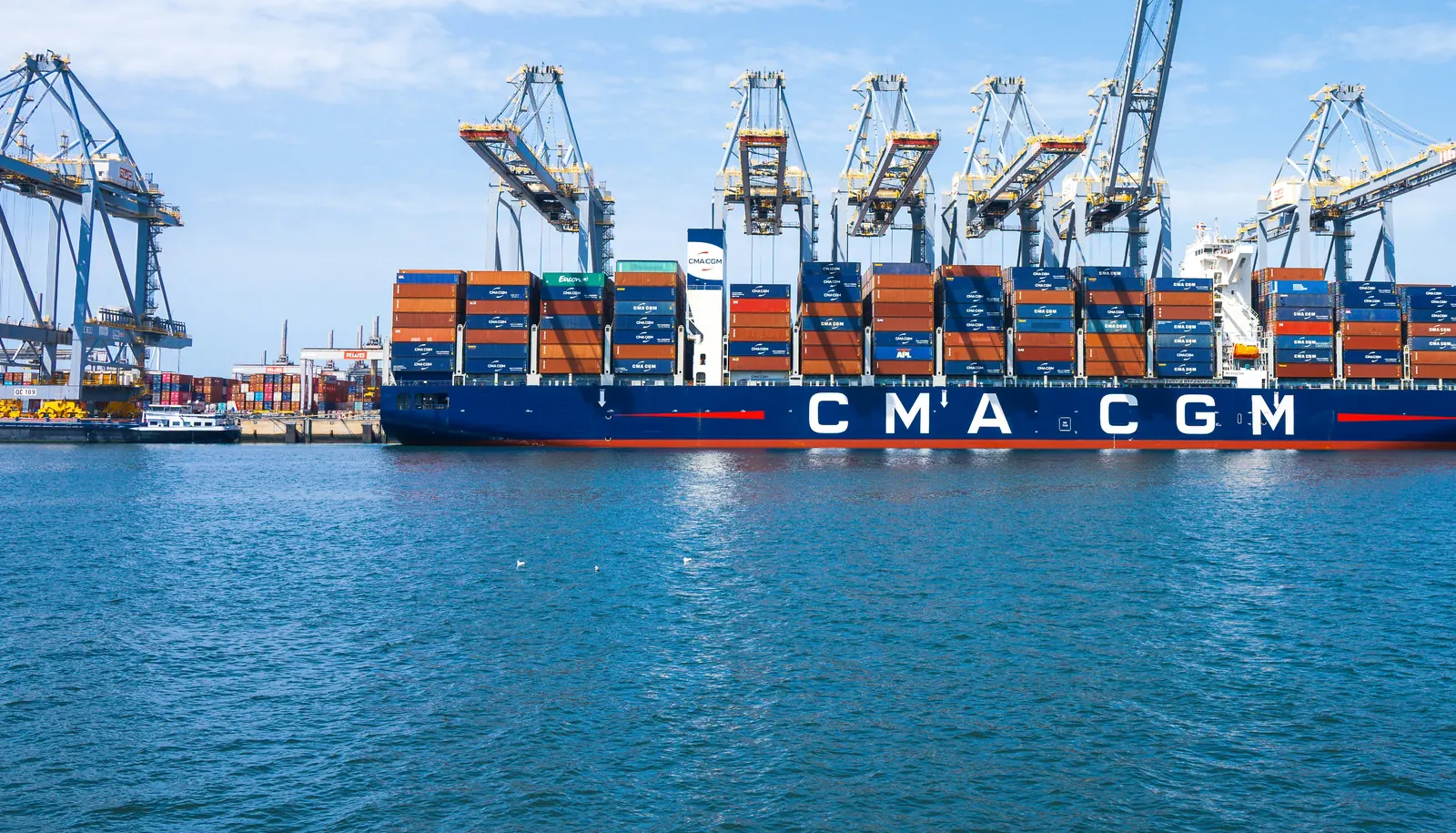 A CMA CGM container ship at a terminal under blue skies, CMA CGM on its hull