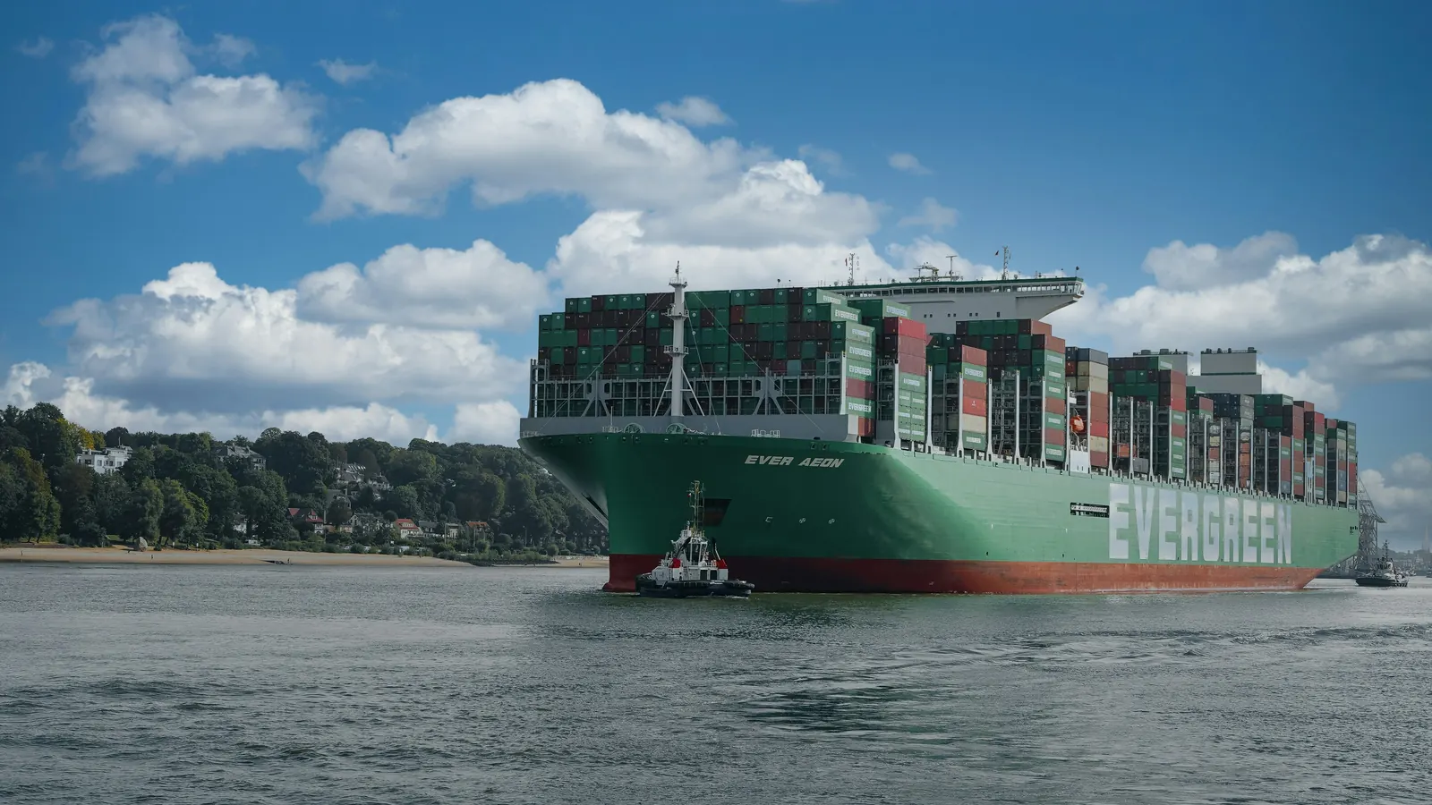 A green Evergreen container ship with a tug on a river, EVERGREEN on its hull