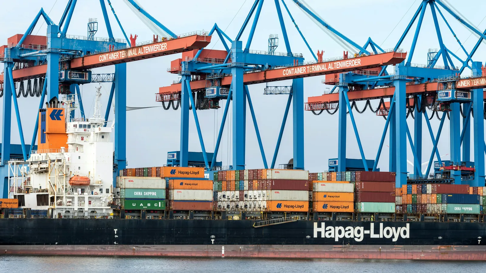 A Hapag-Lloyd container ship under blue gantry cranes, Hapag-Lloyd on its hull