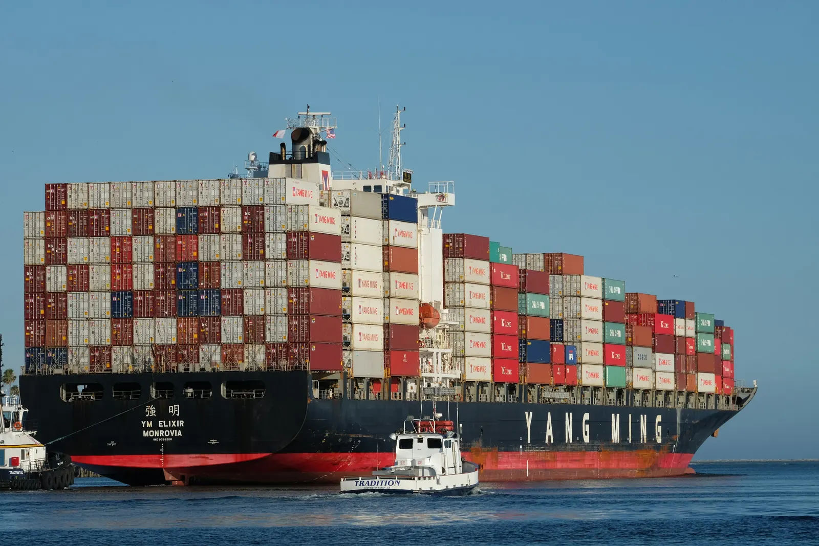 A loaded Yang Ming container ship with a tug alongside, YANG MING on its hull
