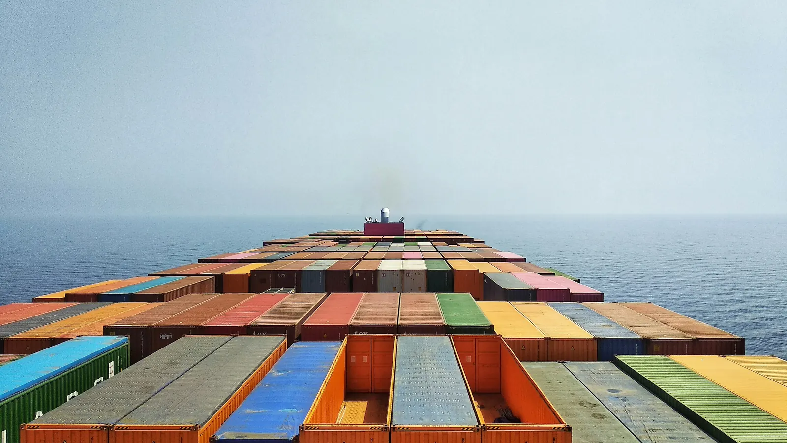 View along the deck of a container ship: rows of containers stretching toward the bridge at sea