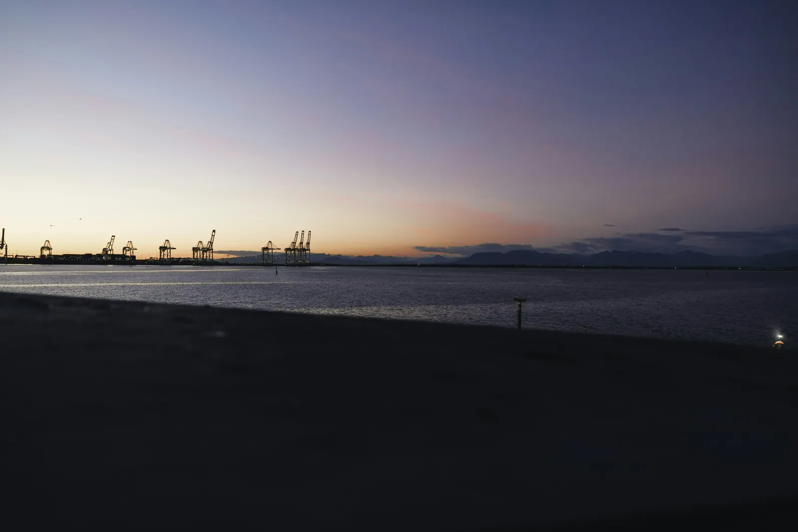 Container cranes on the horizon of a calm harbour at dusk