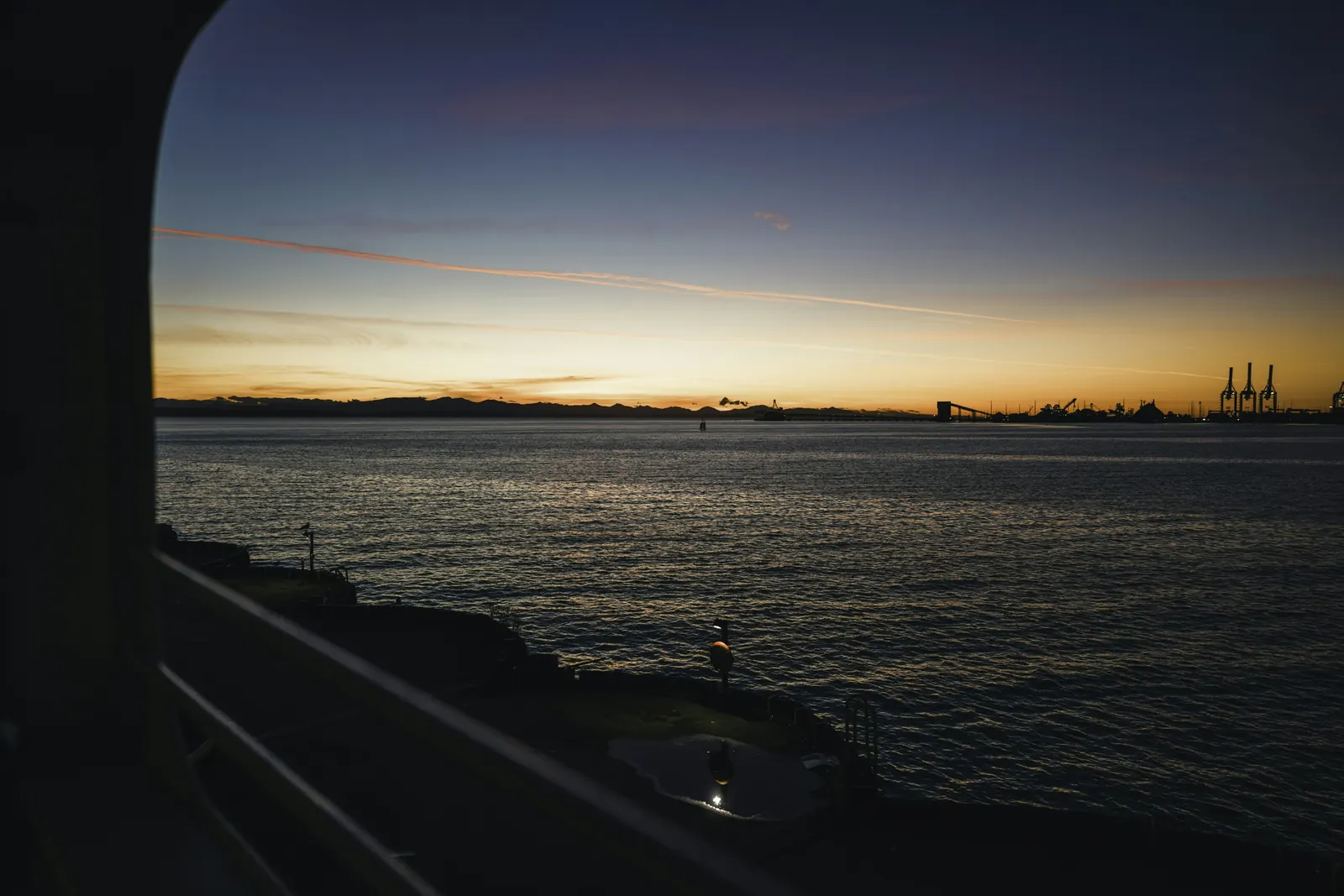 The open sea at sunset with an industrial port faint on the horizon