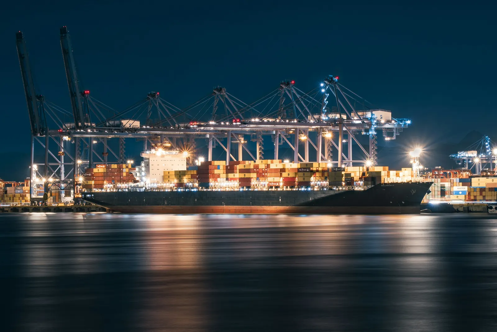A container ship under lit gantry cranes at Yantian Port, Shenzhen, at night