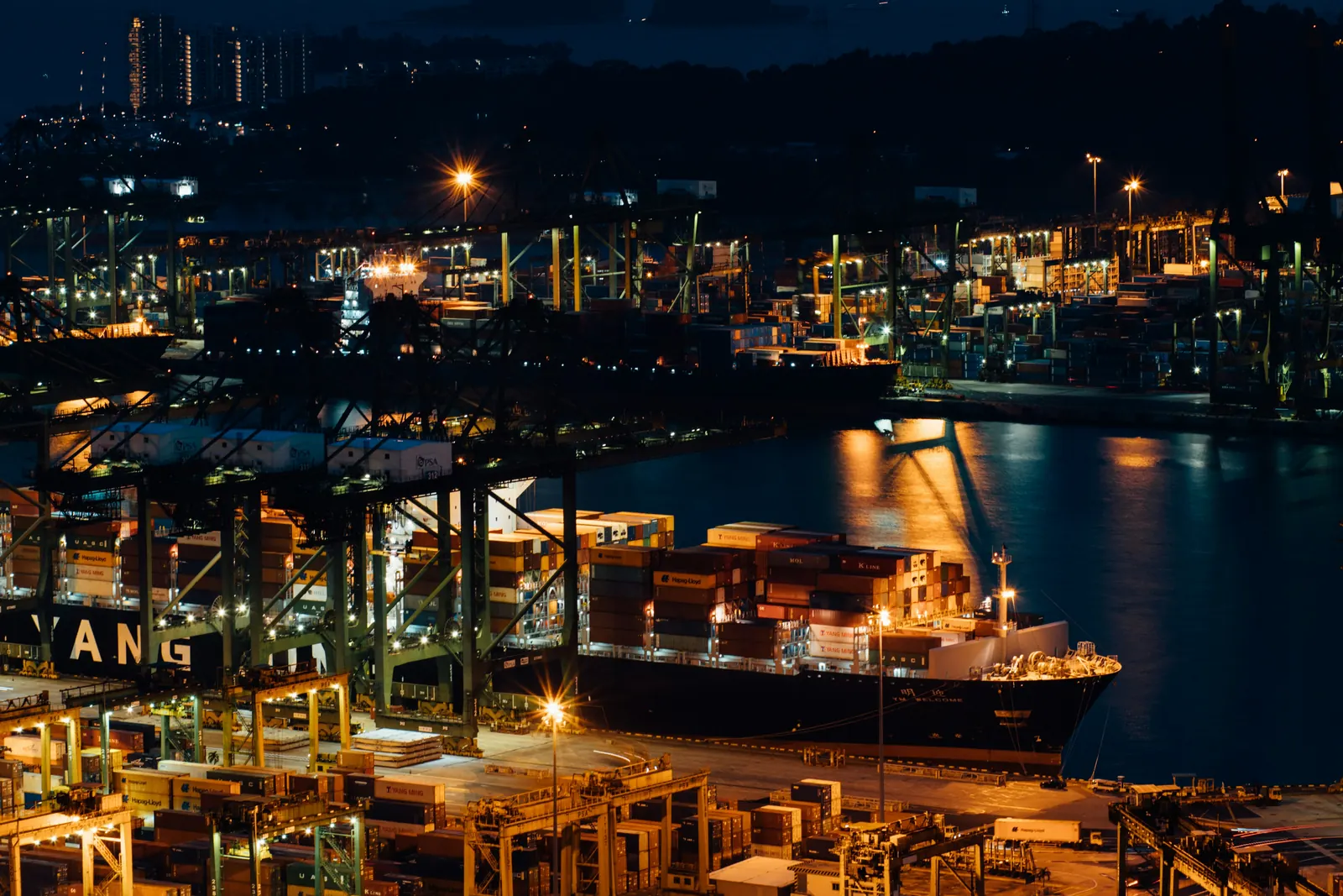 A container terminal in Singapore at night, a ship alongside under floodlights