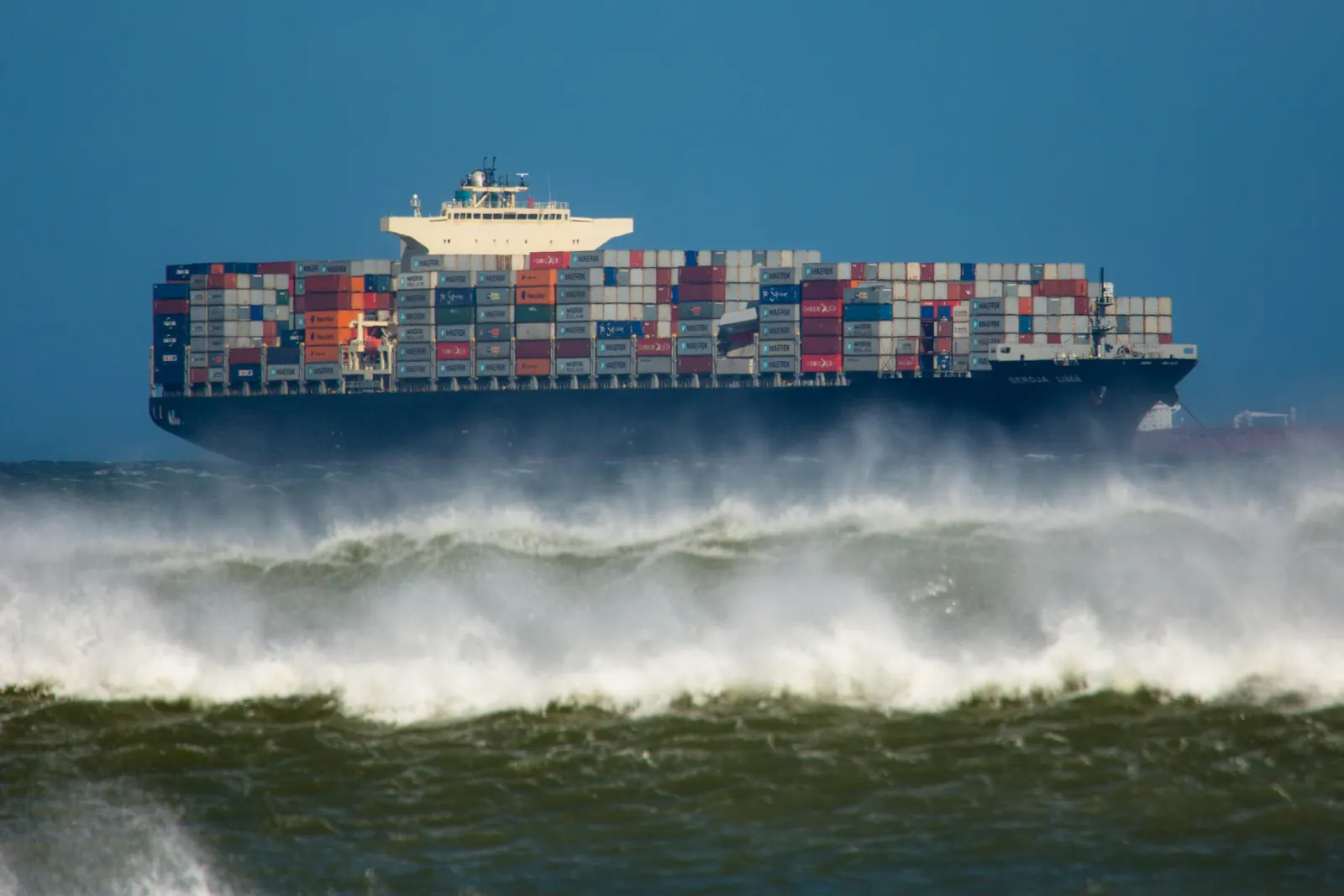 A container ship at sea behind breaking waves