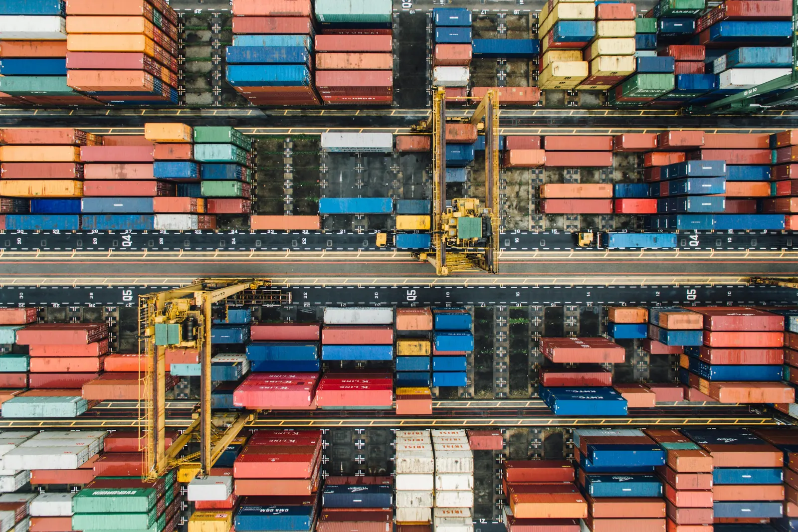Overhead view of colourful containers stacked in yard rows, with yellow gantry cranes over the lanes