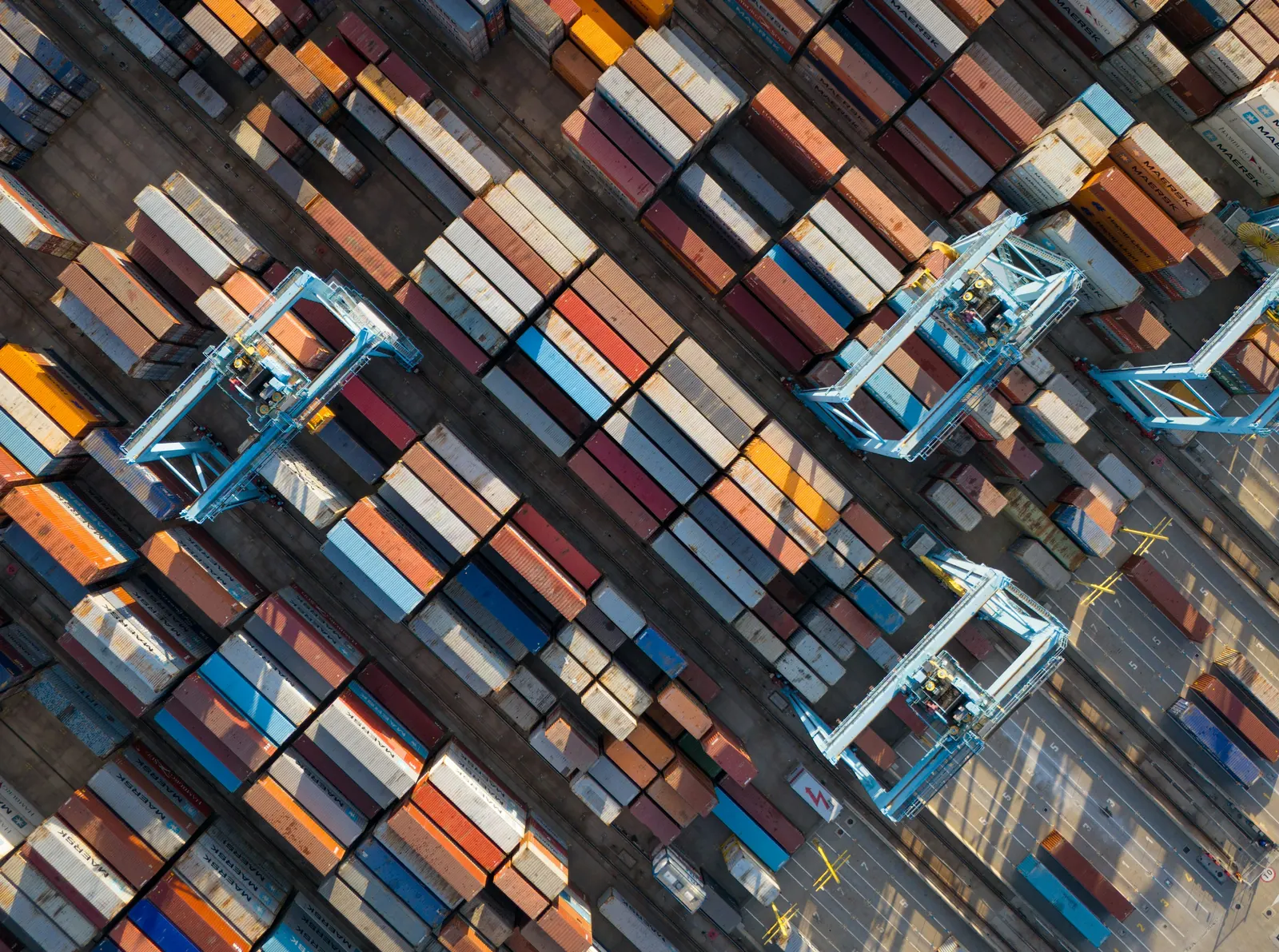 Top-down view of a container yard: rows of stacked containers with gantry cranes between them